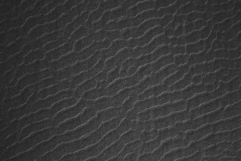 Overhead close-up of wavy ripple patterns in fine dark black sand