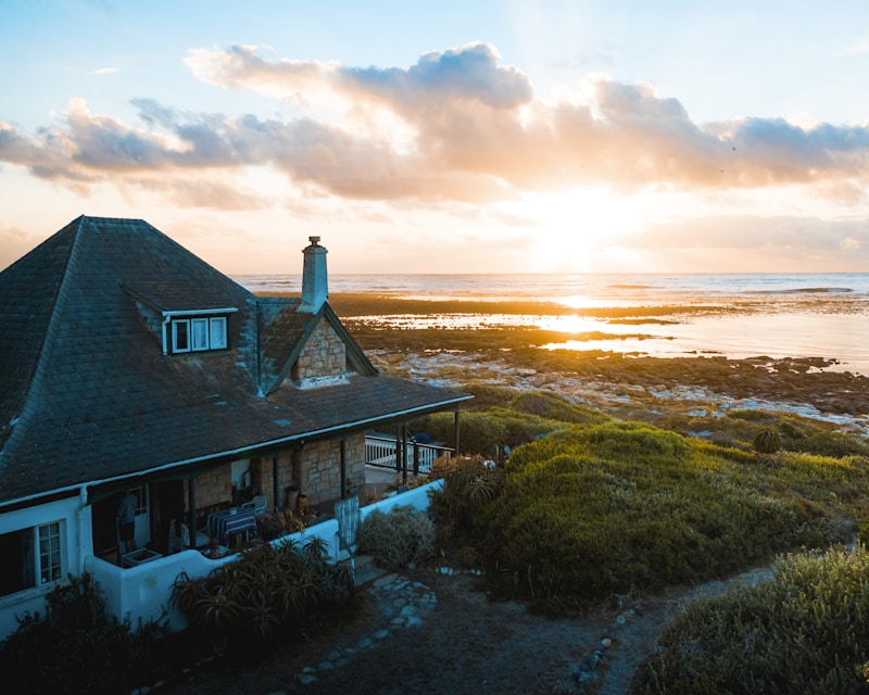 Stone cottage with dark shingle roof on a rocky coastline overlooking the ocean at golden hour sunset